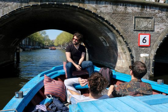 Storyteller Tommy en enkele gasten aan boord van boot Hedir. Rondvaart door de Amsterdamse grachten met Rederij Lampedusa. Vluchtelingen vertellen tijdens de boottocht hun verhaal.