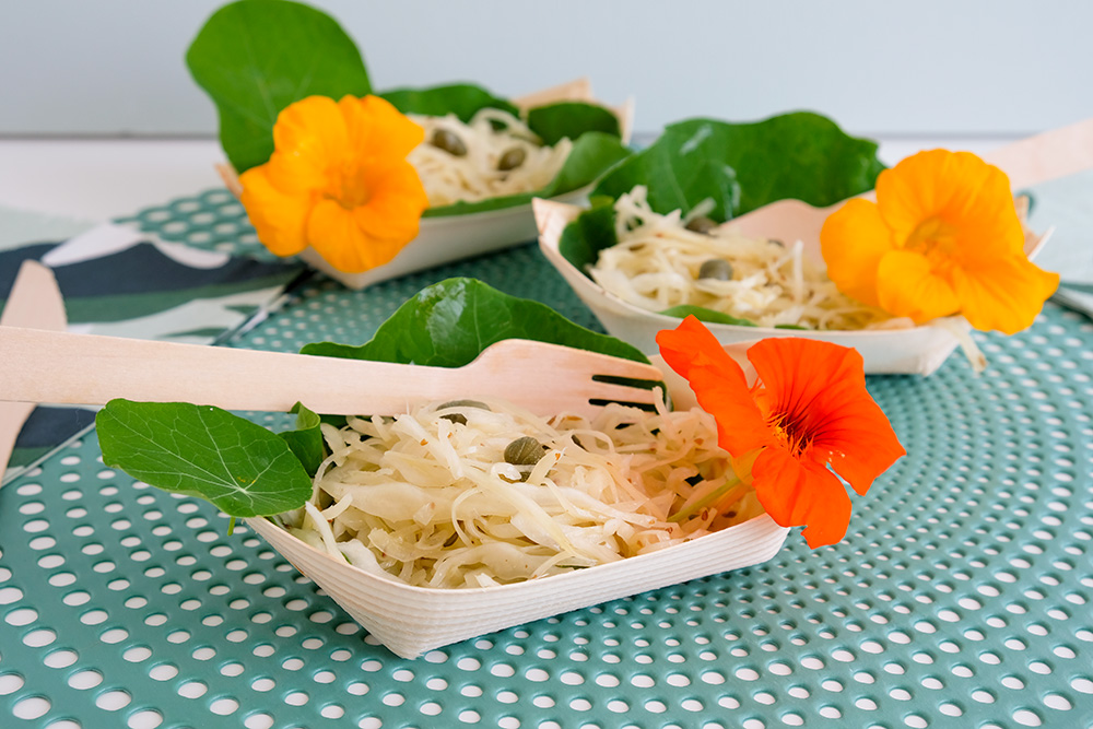 De bloemen van de Oost-Indische kers zijn ook eetbaar. Witte kool-salade op een blad van Oost-Indische kers